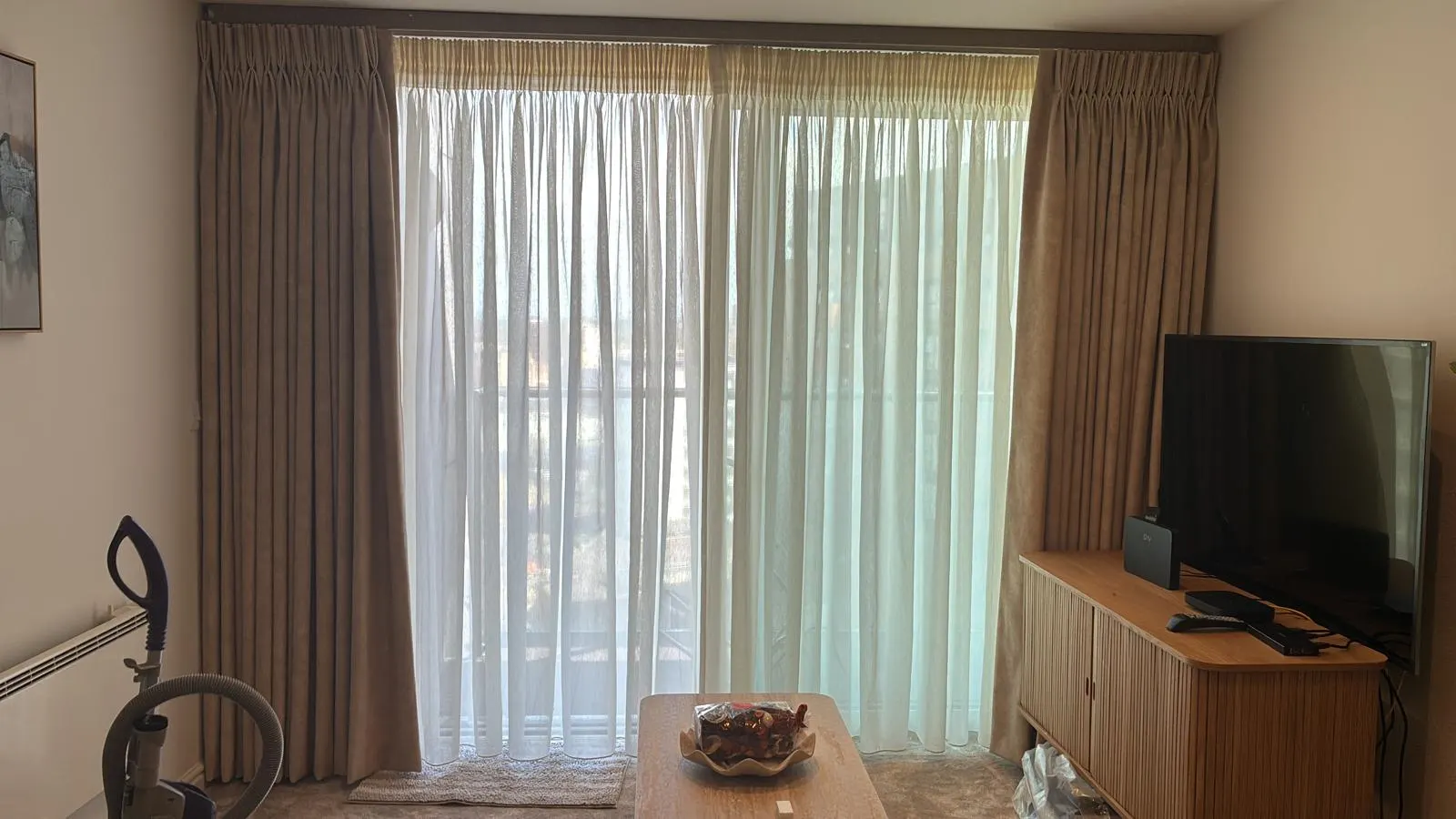 Full-width taupe pinch-pleat curtains and white sheers across a living-room window wall