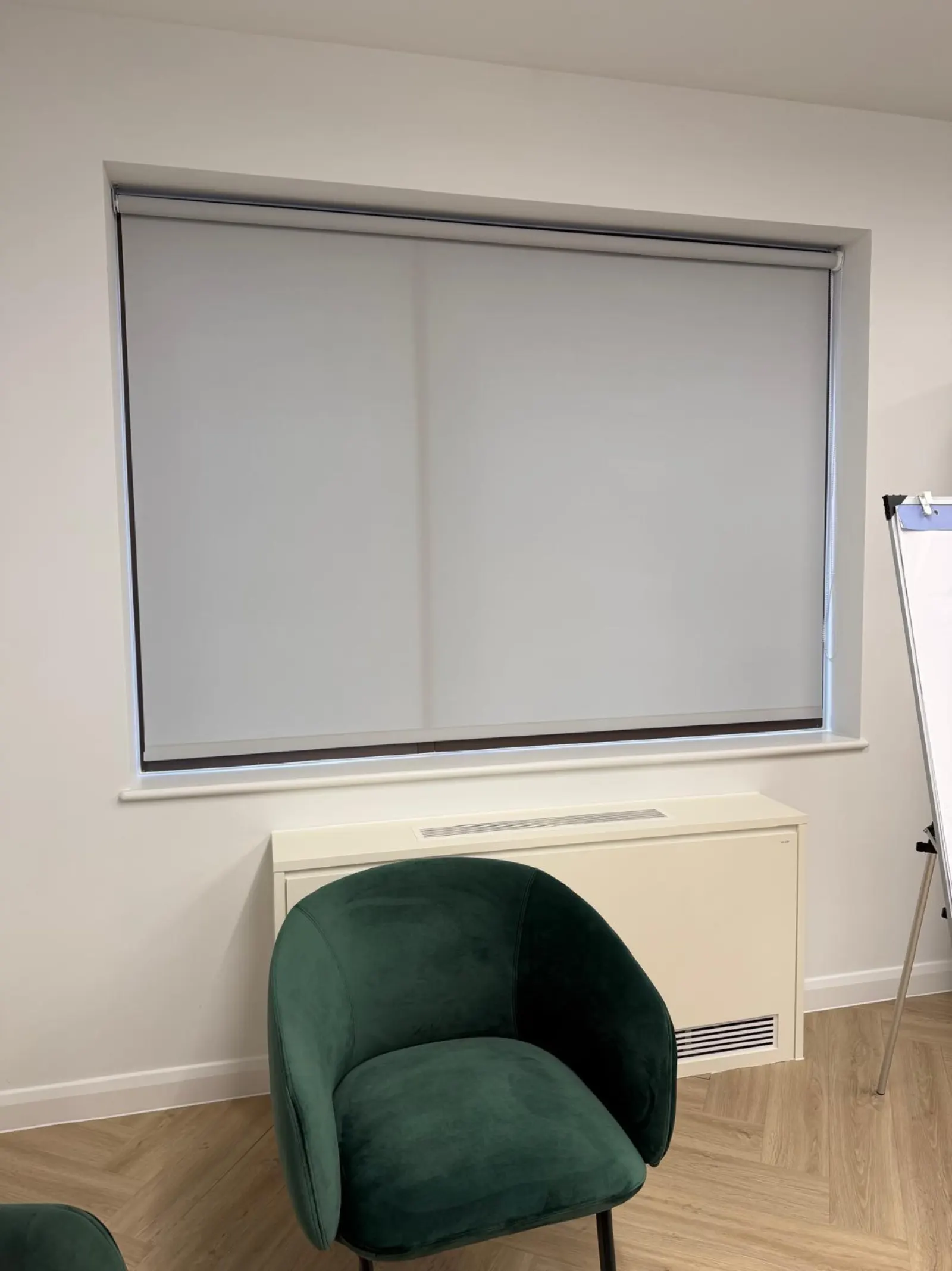 Grey roller blind fitted in a meeting room with a flip chart and green chair